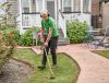 Man trimming grass in a backyard garden with a string trimmer, wearing protective gear for safety