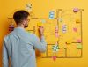 A man creatively arranges colorful post-it notes on a wall, forming a unique design or image
