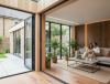 Cozy modern living room with a couple on a sofa, surrounded by plants and natural light from large glass doors.